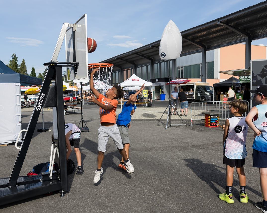 Des enfants jouant au basket sur un terrain extérieur, visant le panier.