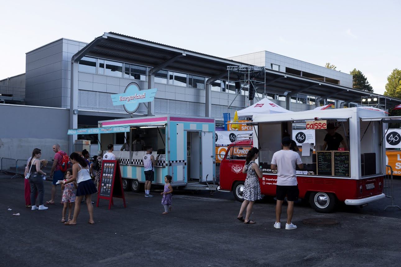 Des food trucks et des personnes appréciant des repas lors d'un rassemblement en plein air.