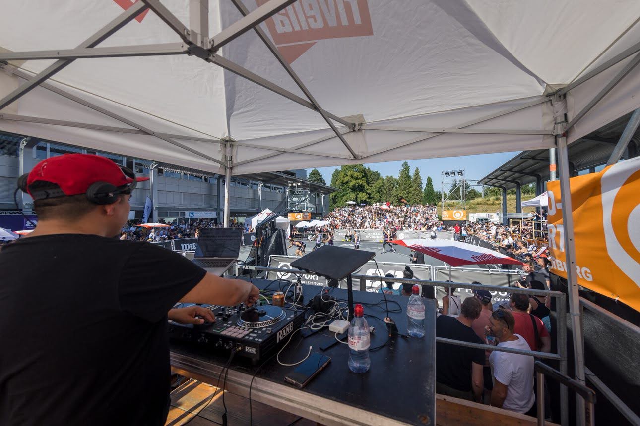 Un DJ jouant de la musique lors d'un événement en plein air, surplombant un terrain de basket animé.